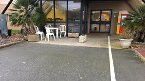 Ein Parkplatz mit weißen Plastikstühlen und -tischen, einer Palme und einem Gebäudeeingang mit Glastür.