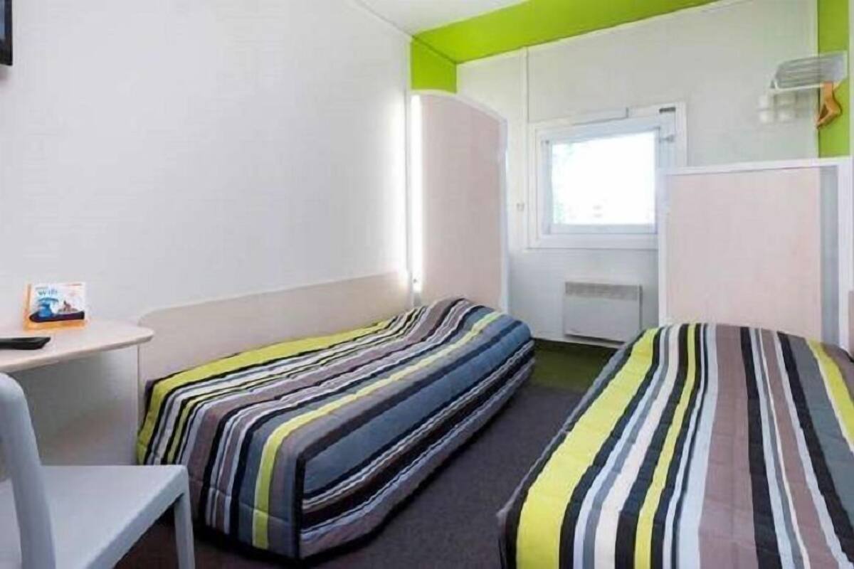 Una habitación pequeña e iluminada con dos camas, un escritorio y una ventana.