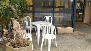 Eine Terrasse mit weißen Plastikstühlen und einem Betonpflanzgefäß mit einer Palme.
