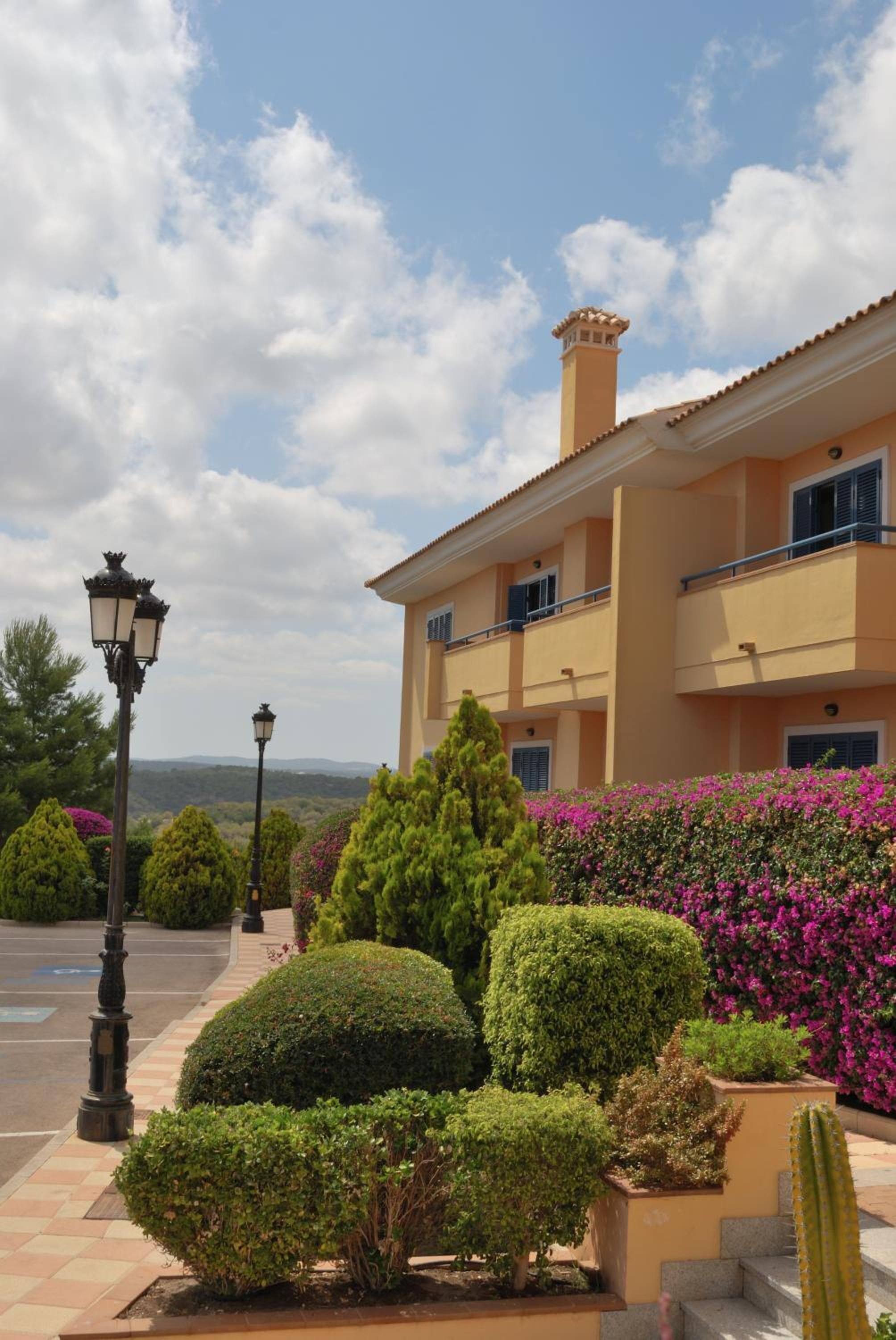 Un edificio de varios pisos con balcones, rodeado de jardines cuidados y cactus.