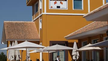 Un bâtiment jaune avec une enseigne indiquant un club de golf, des tables à l’extérieur et des parasols.