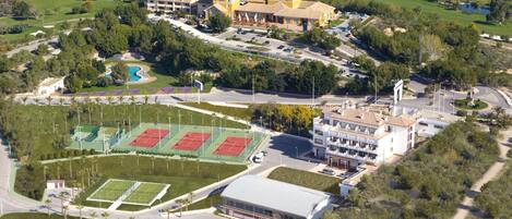 Vista aérea de un campo de golf con un complejo de edificios grande, canchas de tenis y una piscina.