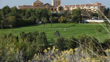 Un hotel grande de varios pisos con una torre central, rodeado de exuberante vegetación y un césped cuidado.