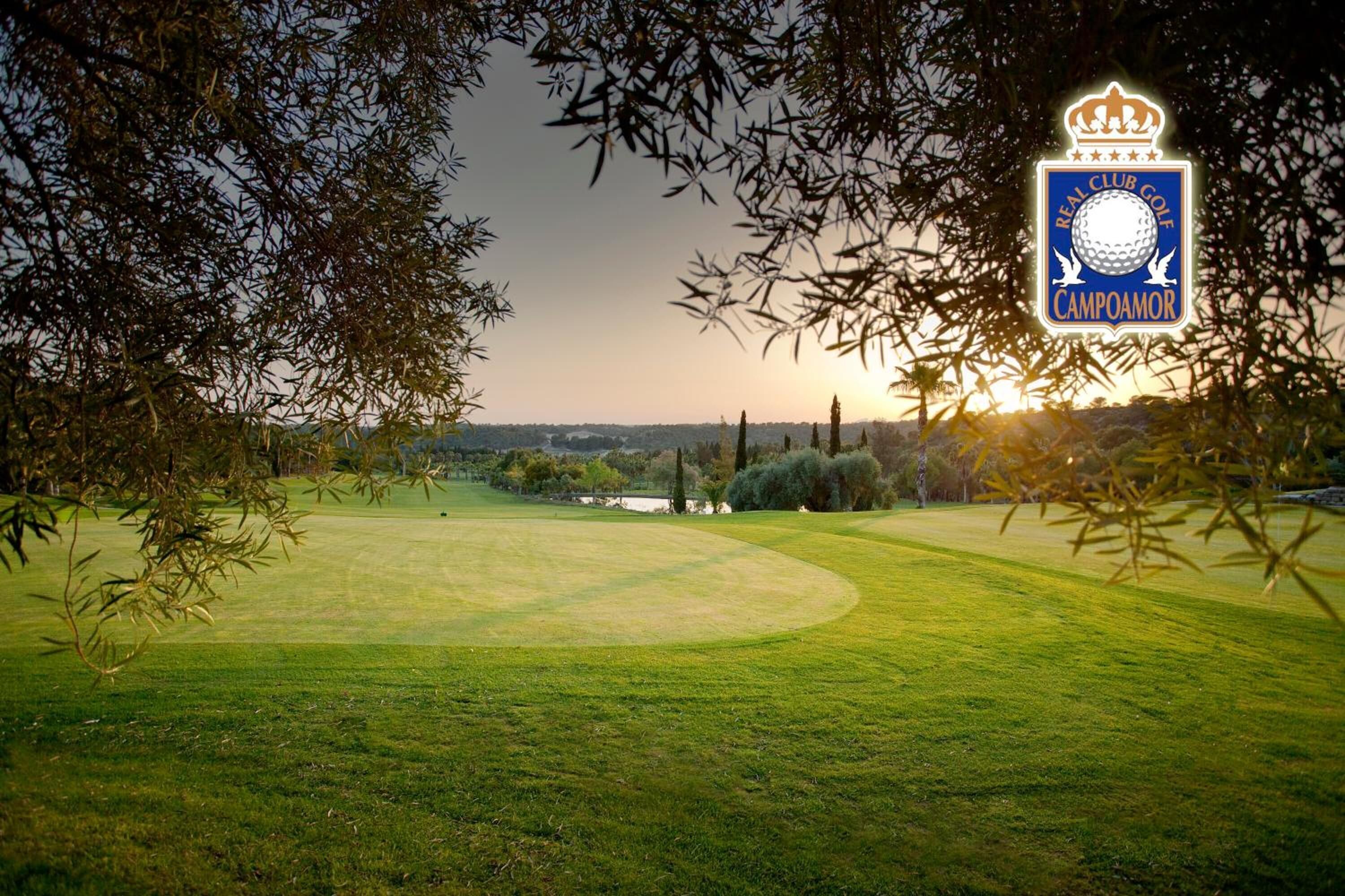 A golf course with a clubhouse logo, surrounded by trees and a sunset in the background.
