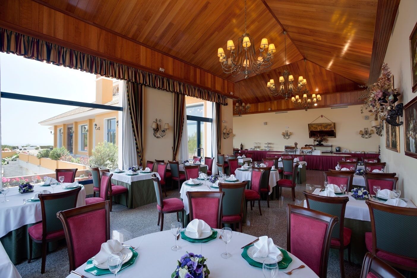 A restaurant with multiple tables, red chairs, and a wooden ceiling.