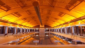 Una amplia piscina interior con varias pistas de natación, rodeada de zonas de estar y un techo alto abovedado.