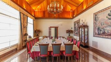 A formal dining room with a long table set for a meal, wooden paneling on the ceiling, and a large tapestry on the wall.