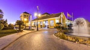 Un hotel con una entrada bien iluminada, una fuente y un cielo despejado.