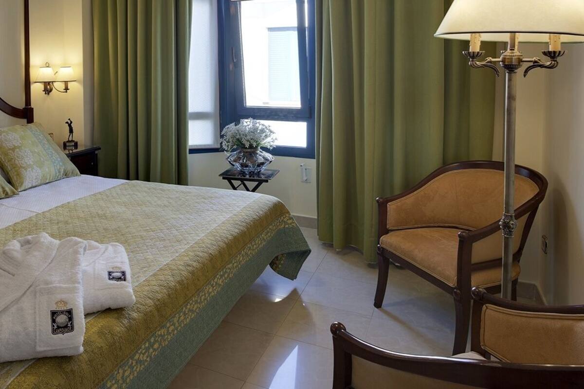 Une chambre d’hôtel avec un lit, une chaise, une lampe et une fenêtre avec des rideaux.