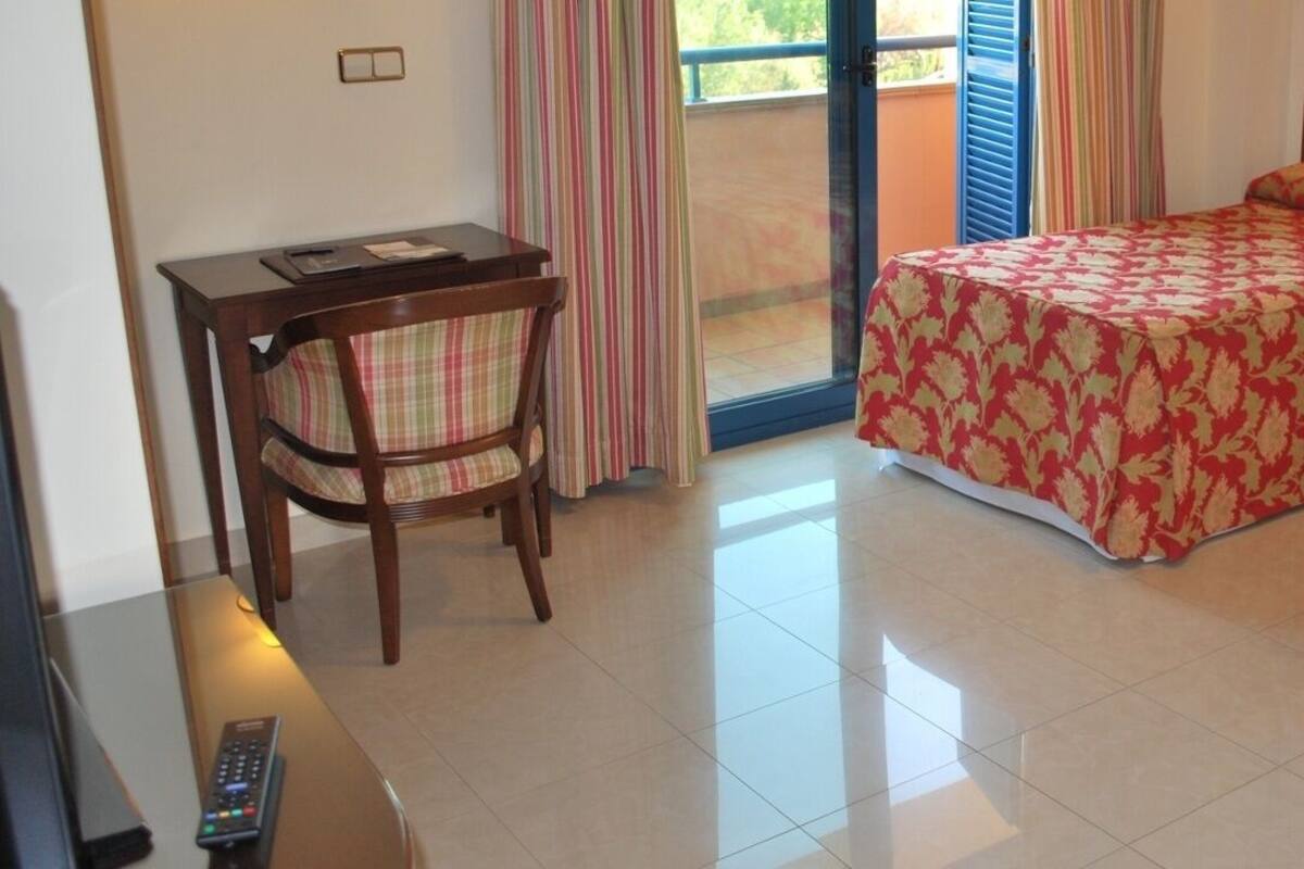 Une chambre d’hôtel avec deux lits, un bureau, une chaise et un balcon avec des rideaux.