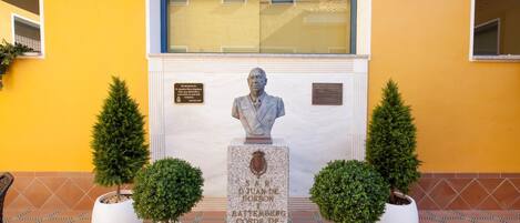 A statue of a man in a suit, surrounded by potted plants, with a plaque in front.