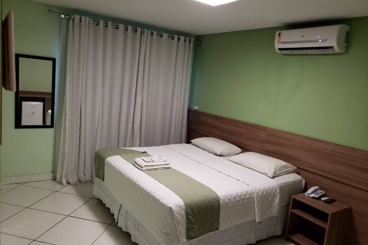 A hotel room with a bed, a bedside table with a phone, and an air conditioning unit.