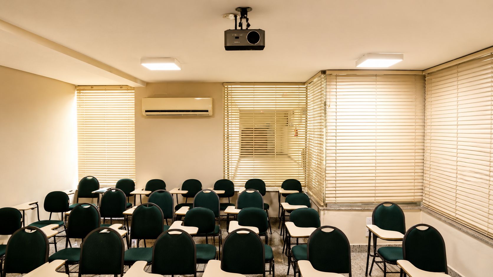 Une salle de conférence avec des rangées de chaises, un projecteur et un appareil de climatisation.