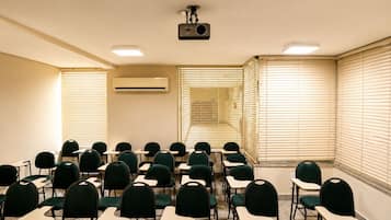 Un salón de conferencias con filas de sillas, un proyector y un equipo de aire acondicionado.