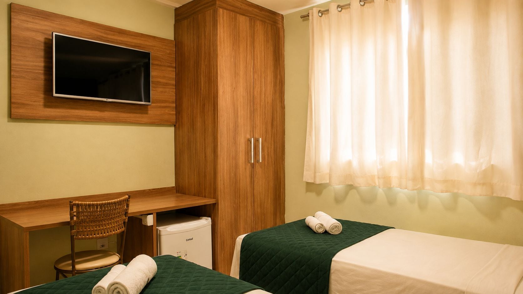 Habitación de hotel con cama, escritorio, silla, televisor y ventana con cortinas.