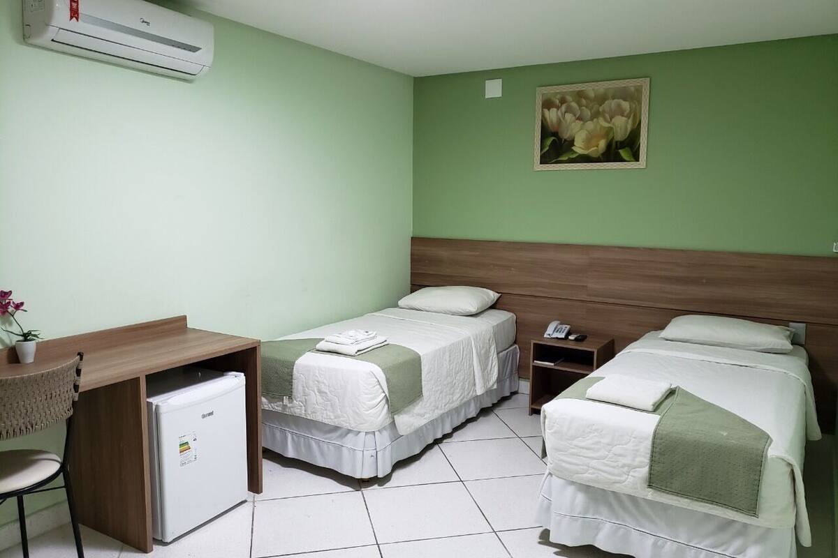 A room with two beds, a desk, a refrigerator, and a wall-mounted air conditioner.