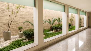 Un pasillo con una serie de ventanas, cada una con vistas a un jardín ajardinado con diversas plantas y un suelo cubierto de guijarros.