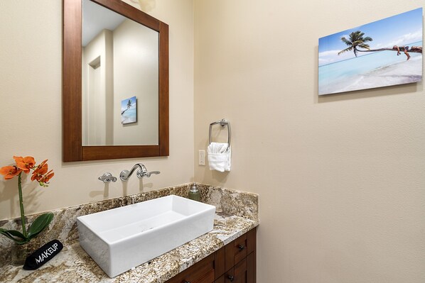 Un baño con un lavabo blanco, un espejo, un perchero para toallas y un cuadro de una playa.