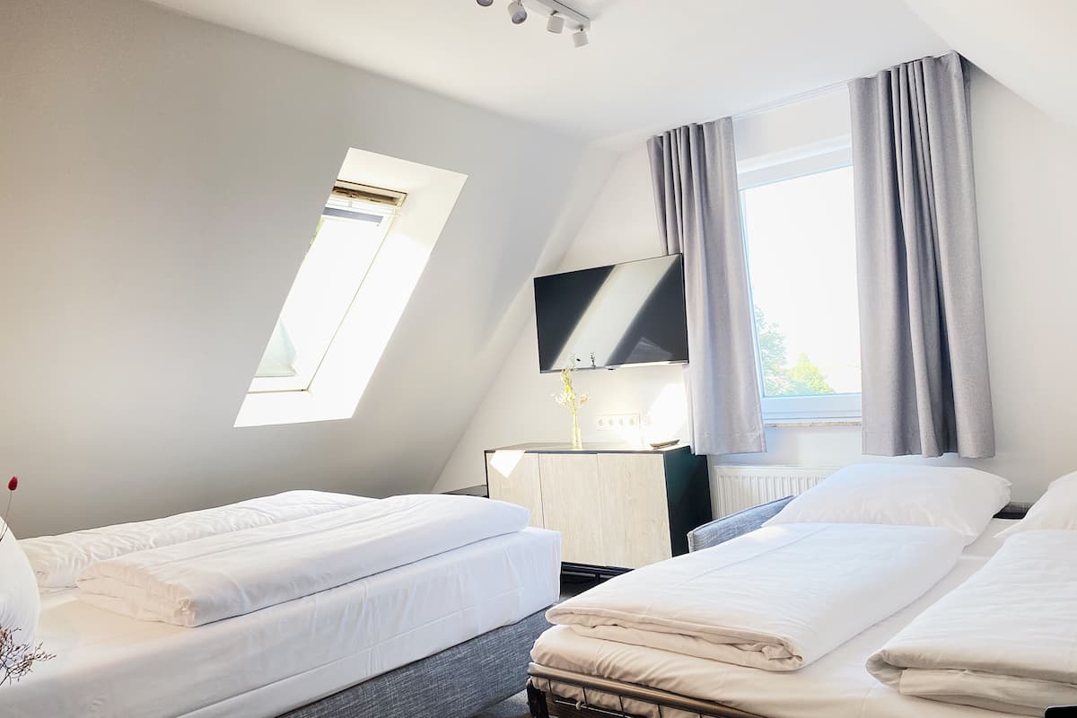 Ein Hotelzimmer mit zwei Betten, einem Fernseher, einem Schreibtisch und einem Fenster mit Vorhängen.