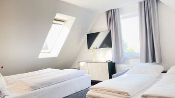 Ein Hotelzimmer mit zwei Betten, einem Fernseher, einem Schreibtisch und einem Fenster mit Vorhängen.