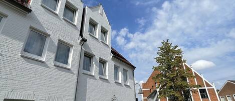 A white brick building with multiple windows and a cobblestone street.