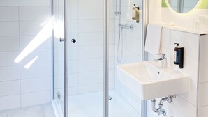 Un baño moderno con ducha de vidrio, un lavabo blanco y un espejo con luz circular.