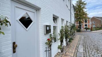 A white brick building with a cobblestone pathway, a white door, and a small window.