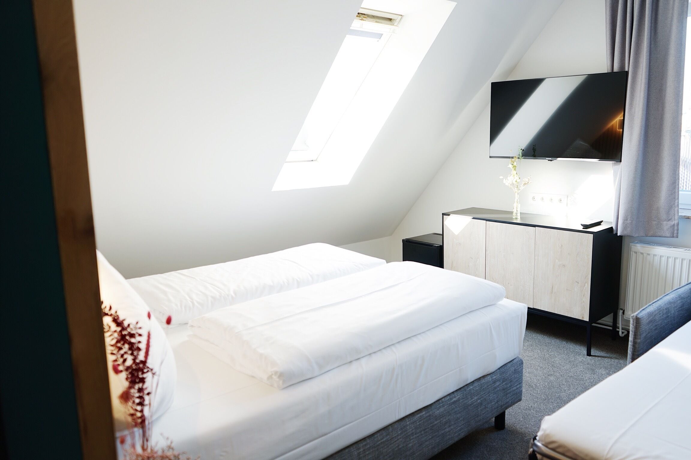 Quarto com cama, mesa de cabeceira, televisão e janela.