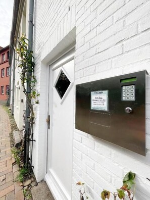 A hotel entrance with a keypad door lock, a sign indicating room availability, and a brick pathway leading to the door. - Hotel Xenia (Flensburg)