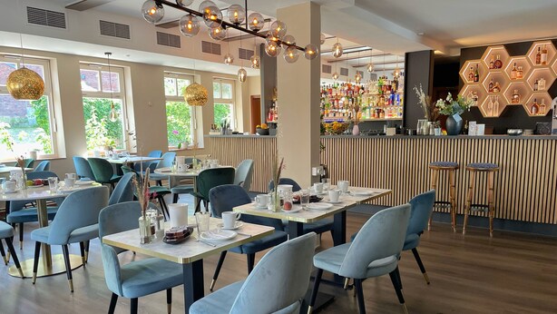 Un interior de restaurante moderno con mesas redondas, sillas azules y una zona de bar con lámparas hexagonales.