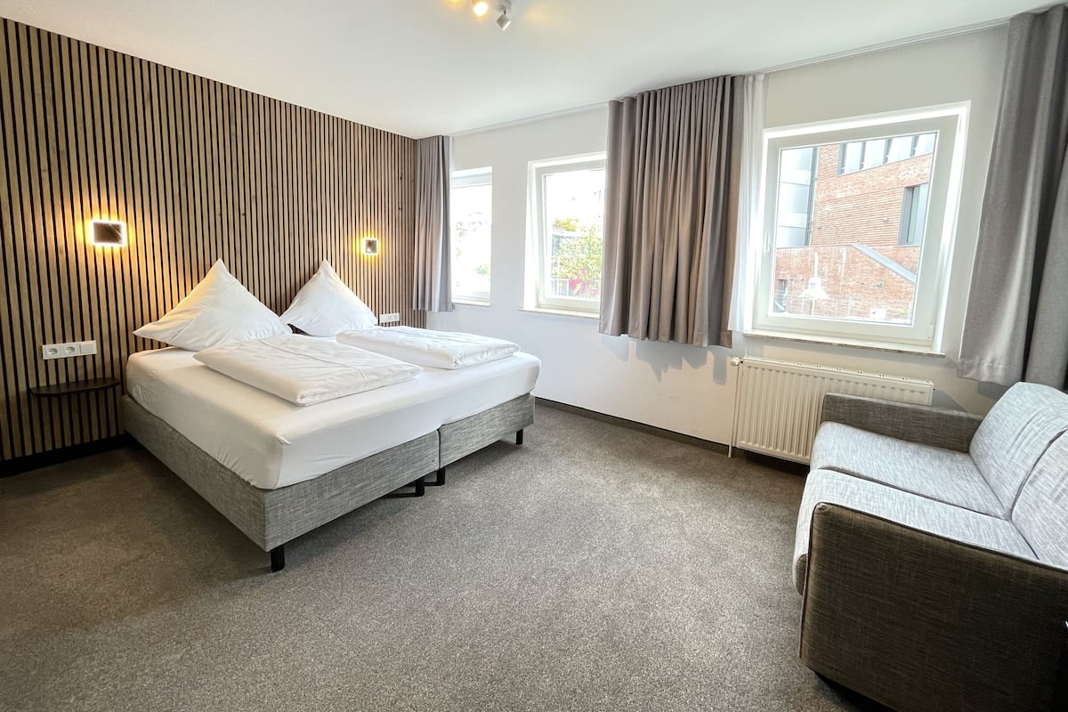 Ein modernes Hotelzimmer mit einem großen Bett, einer Couch und Blick auf die Stadt.