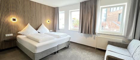 A modern hotel room with a large bed, a sofa, and a view of the city.