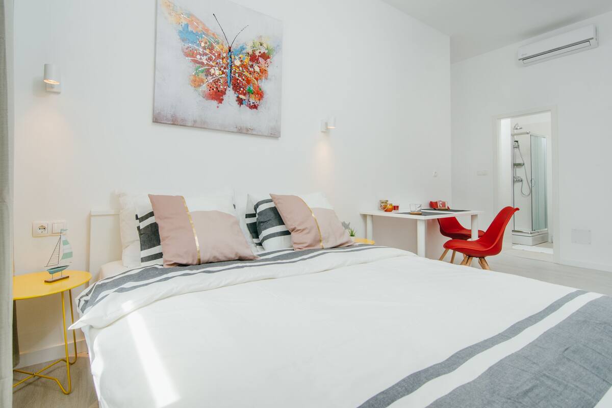 A modern hotel room with a large bed, a small desk, and a red chair.