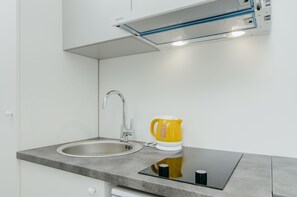 A modern kitchen with a built-in sink, a stainless steel faucet, a yellow electric kettle, and a black induction cooktop.