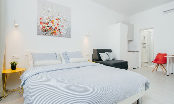 A modern bedroom with a large bed, a grey sofa, a red chair, and a small table.