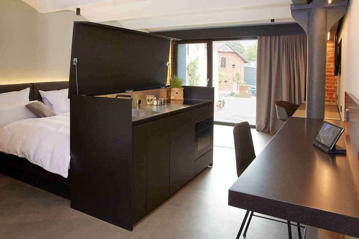 A compact hotel room with a bed, kitchenette, and a dining area.