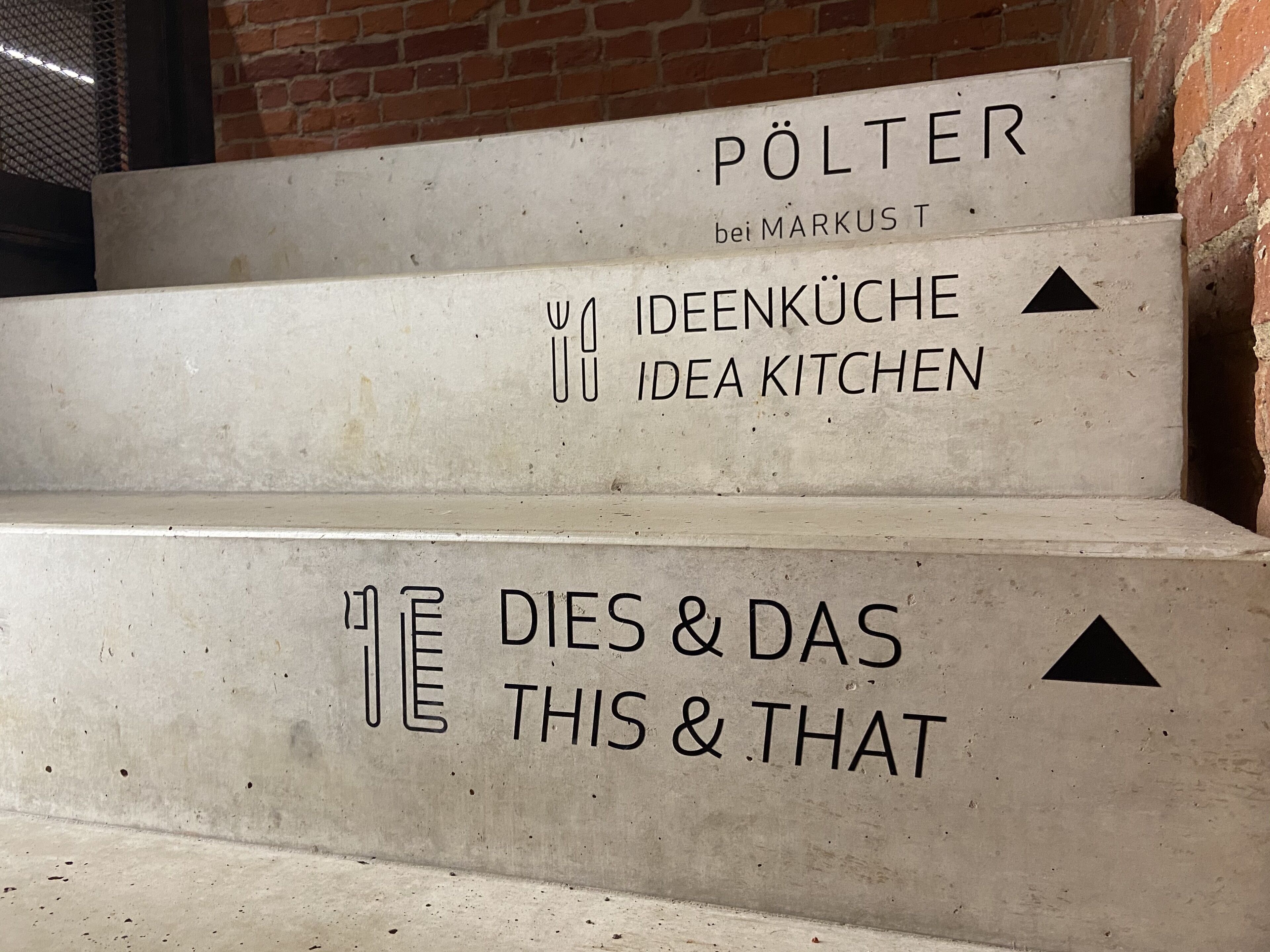 A staircase with steps labeled 'PÖLTER bei MARKUS', 'IDEENKÜCHE IDEA KITCHEN', and 'DIES & DAS THIS & THAT'.