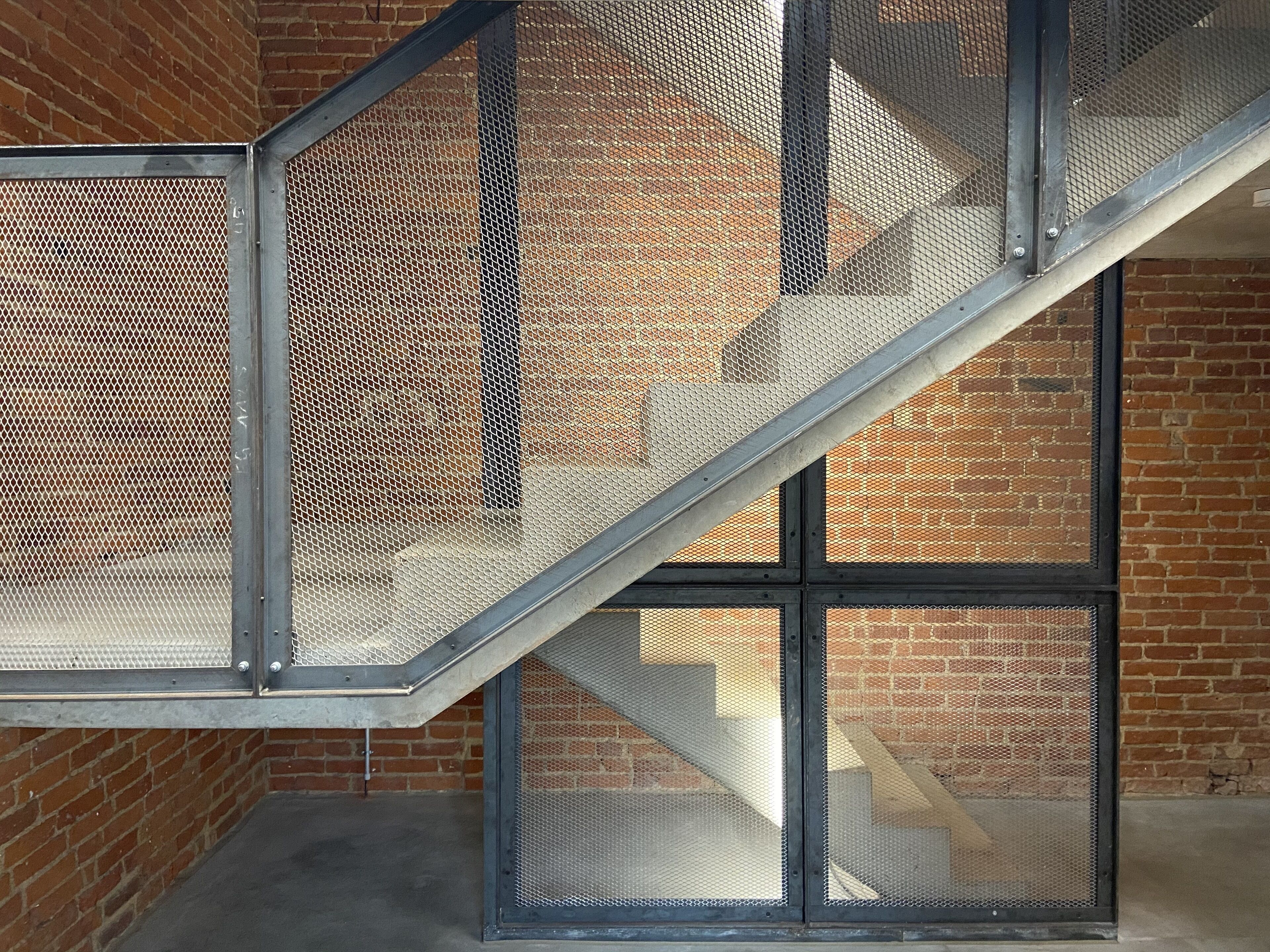 A staircase with metal railings and mesh panels, leading to a brick wall.