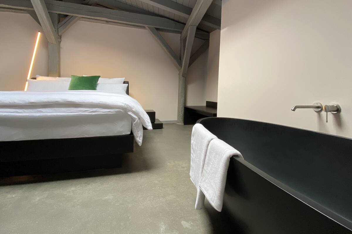 A modern bedroom with a large bed, a black bathtub, and a white towel hanging on the wall.