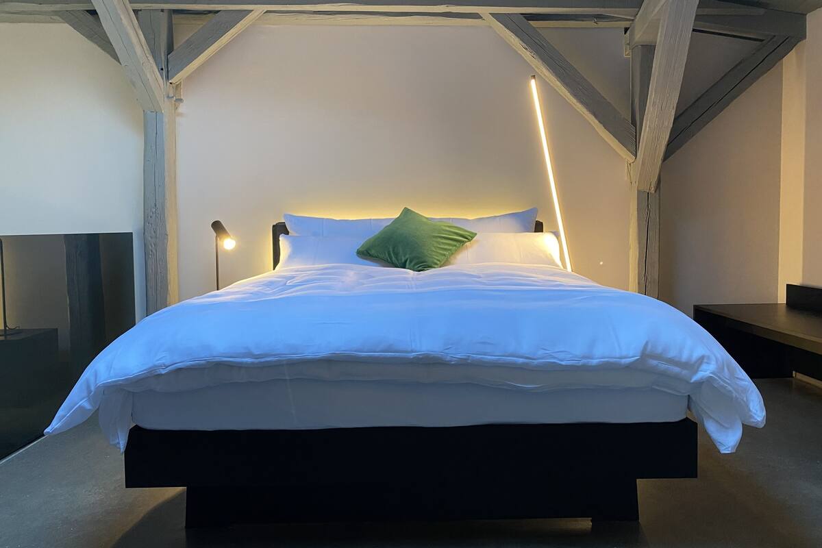 A modern bedroom with a large bed, a headboard with integrated lighting, and a minimalist design.