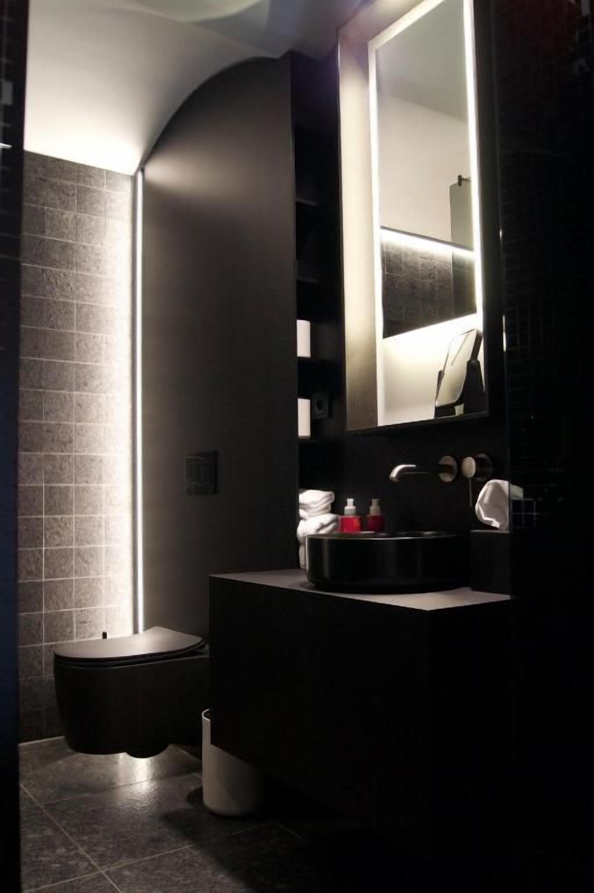 A modern bathroom with a dark-toned sink, a mirror, and a toilet.