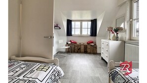 Un dormitori amb llit, escriptori, cadira, finestra amb cortines i radiador.