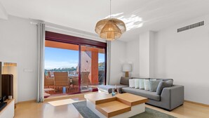A modern living room with a grey sofa, wooden coffee table, and a view through a glass door to an outdoor seating area.