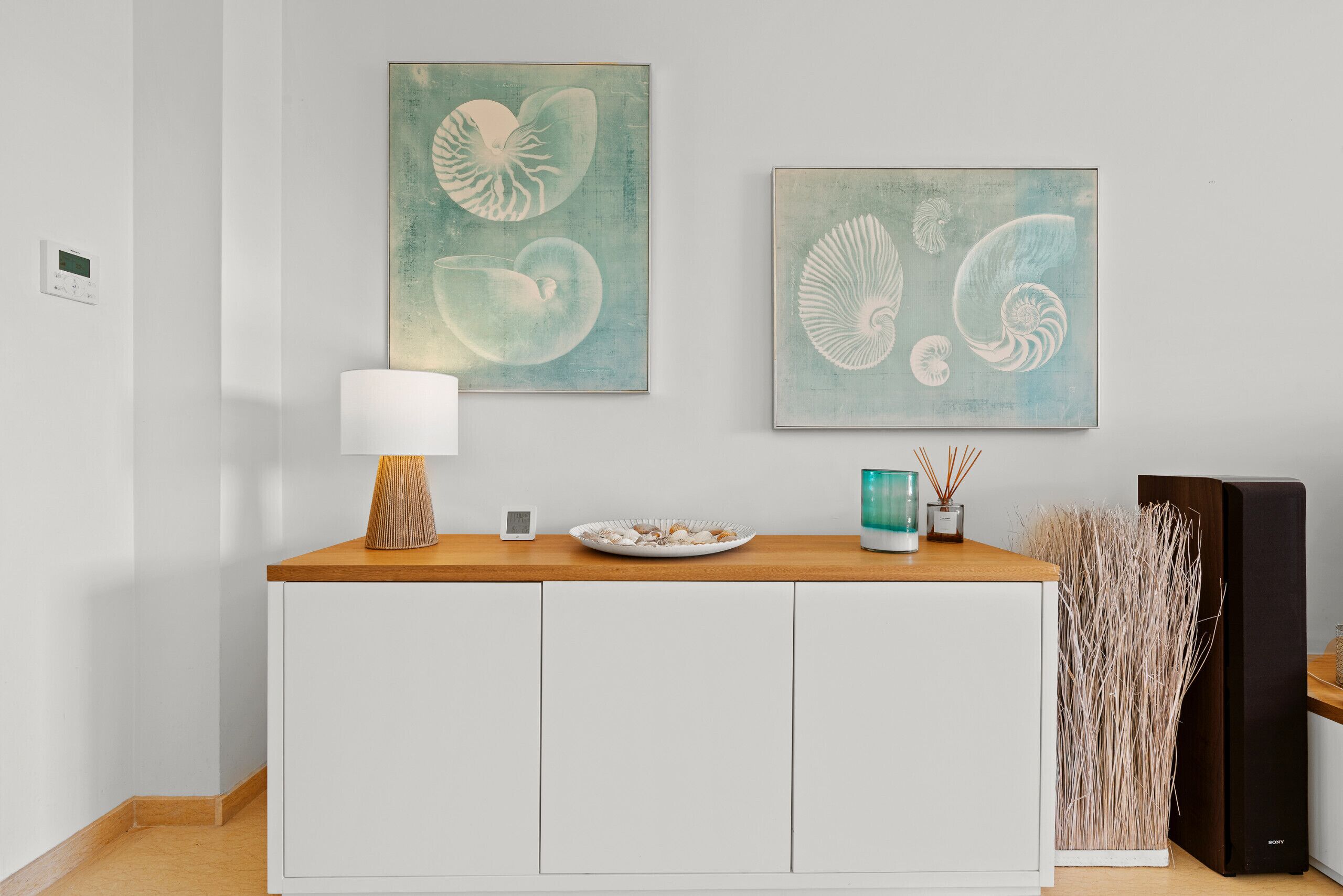Ein modernes Wohnzimmer mit einem Holzkonsolentisch, einem weißen Schrank, einer Lampe und zwei gerahmten Kunstwerken an der Wand.