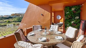 A round table set for dining with wicker chairs, a clock, and a wall decorated with greenery.