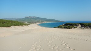 A beach with footprints leading to the water, a mountain in the background, and a clear sky.