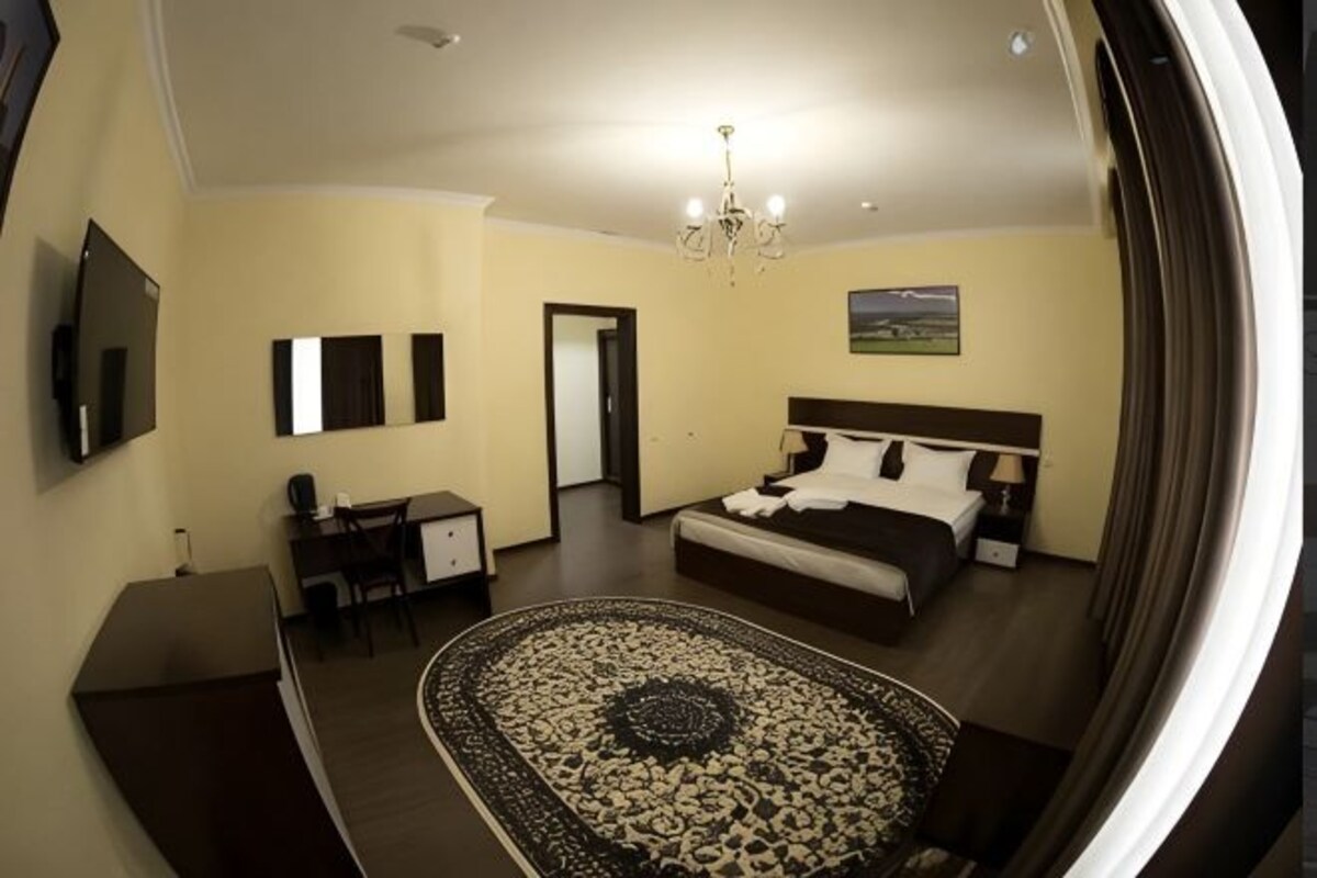A bedroom with a bed, a desk, a chair, a TV, and a chandelier.