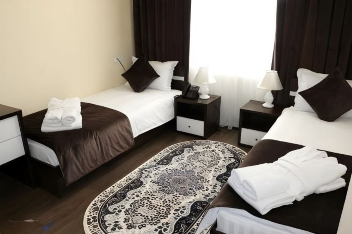 A hotel room with two beds, a nightstand with a lamp, a bedside table, and a patterned rug.