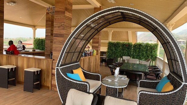 A cozy outdoor seating area with wicker furniture and a bar in the background. - Nimi Beach Resort (Freetown)