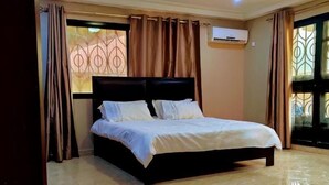 A bedroom with a large bed, a ceiling light, and a window with curtains. - Nimi Beach Resort (Freetown)